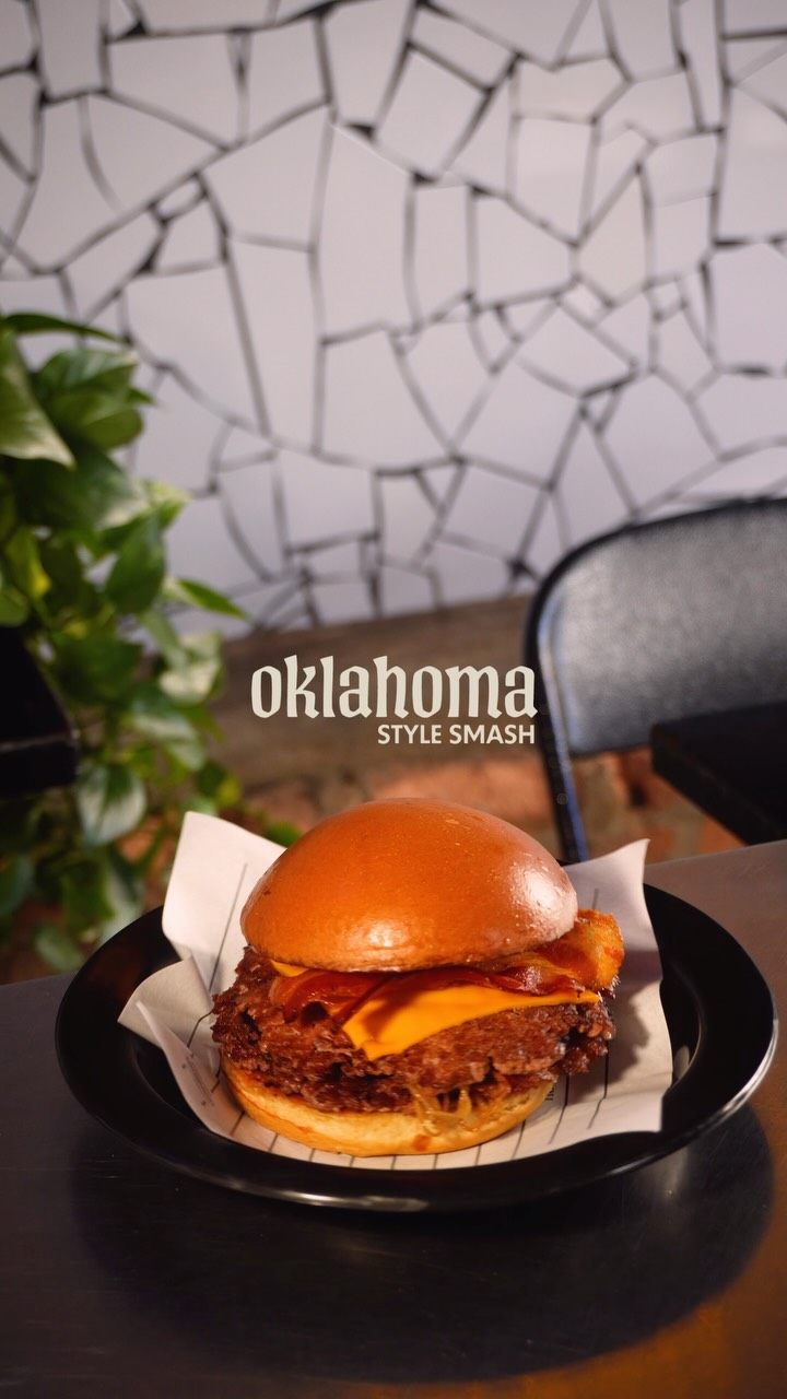 Oklahoma Style Smash com cheddar e bacon no prato preto, na frente da parede de mosaico