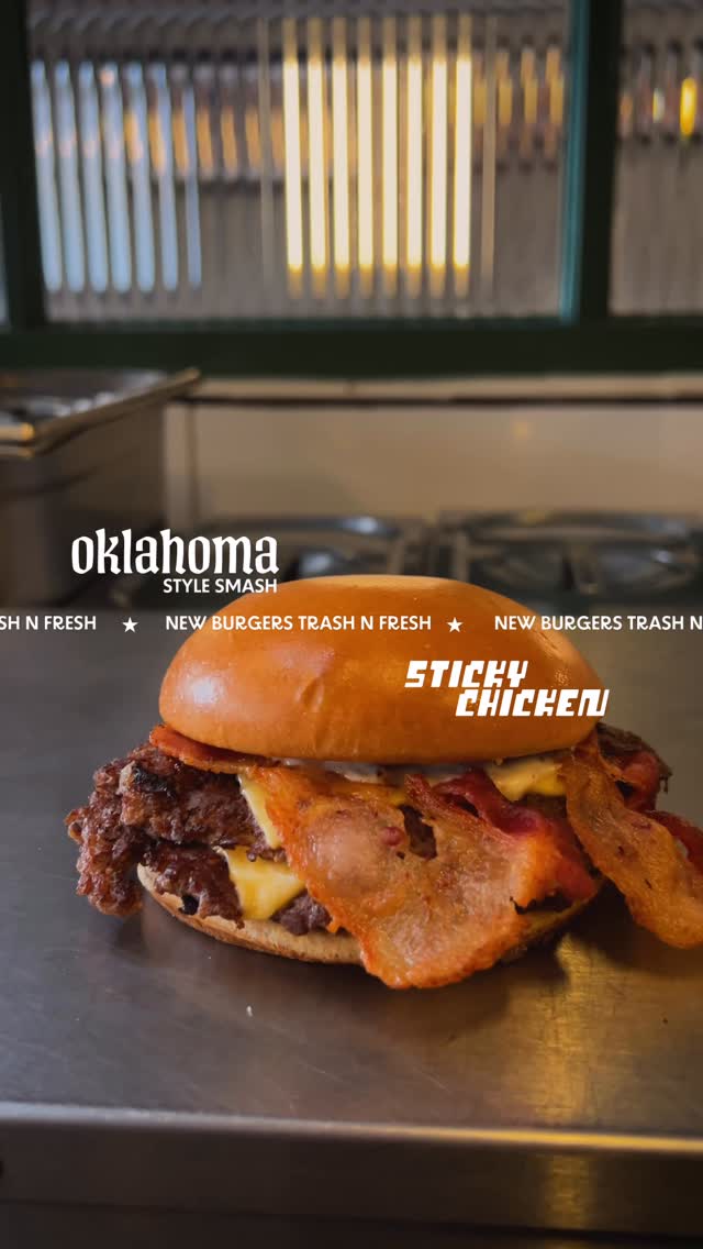Oklahoma Style Smash com muito bacon sobre a bancada de inox, com faixa New burgers Trash n Fresh
