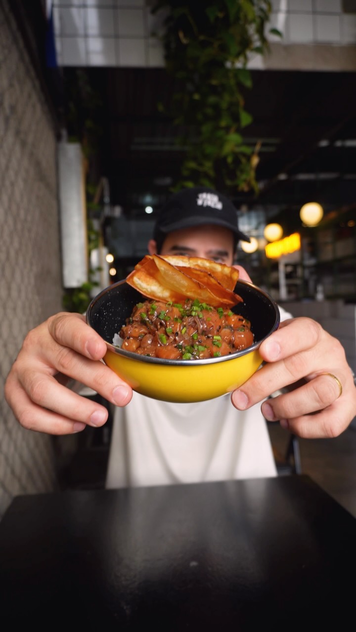 Rapaz de boné segurando a tigela amarela do Poke Original Havaiano, com salmão marinado e chips de batata-doce