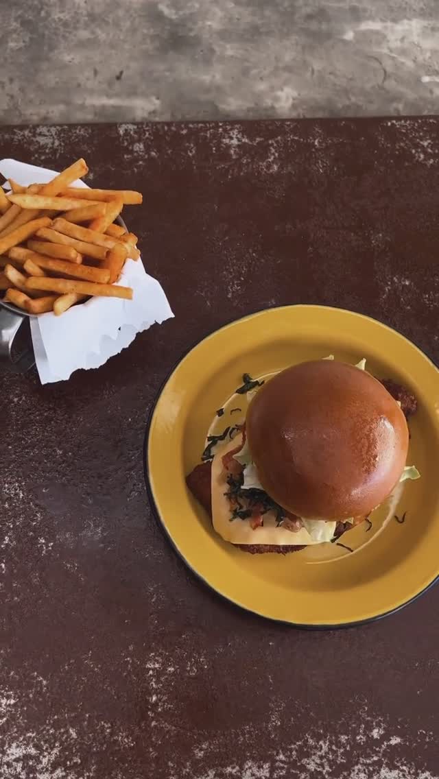 Vista de cima: burger no prato de ágata amarelo e batata frita na cestinha de metal com papel, sobre a mesa de ferro cor de ferrugem
